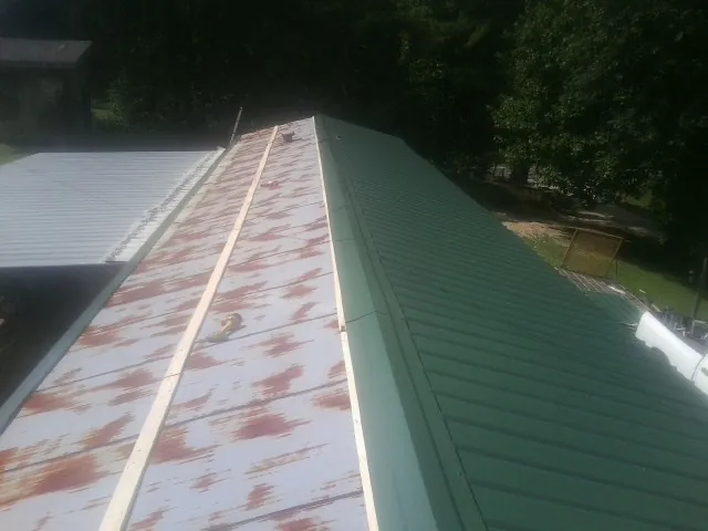 Old rusted panels beside newly installed green metal roofing — Wind Damage Roof Repair by Roofing Brothers in Springville