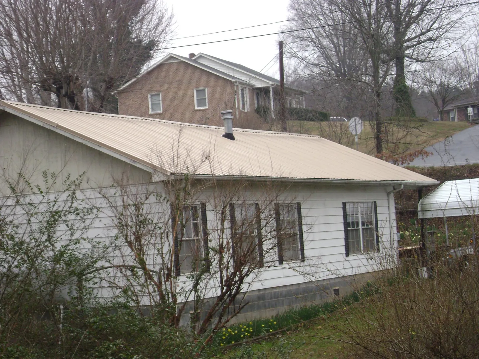 Tan metal roof on a white sided house set into a hillside — Commercial Roofing by Roofing Brothers in Springville